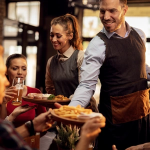 Happy waiters bringing food table serving group friends restaurant